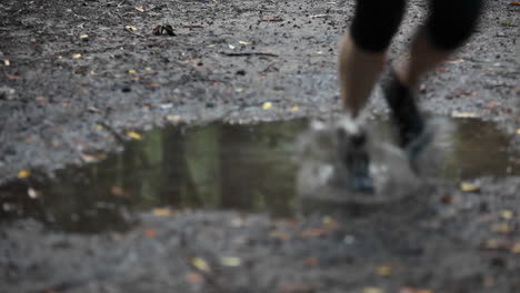 A-woman-jogs-over-a-puddle-reflecting-the-woods-of-the-area-where-she-is