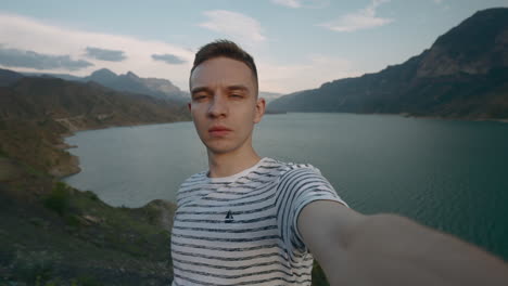 man taking selfie by a lake surrounded by mountains