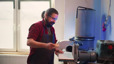 Manufacturer-shaping-wooden-bowl-on-disc-sander-in-assembling-shop