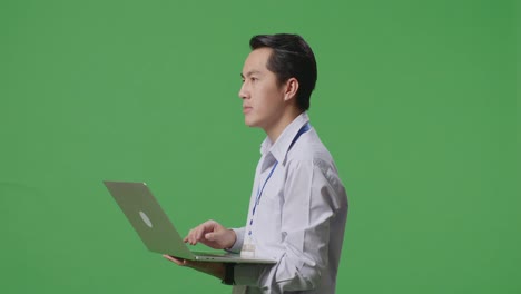 아시아 사업가 가 노트북 컴퓨터 를 사용 하고 스튜디오 의 초록색 스크린 배경 을 둘러보고 있다