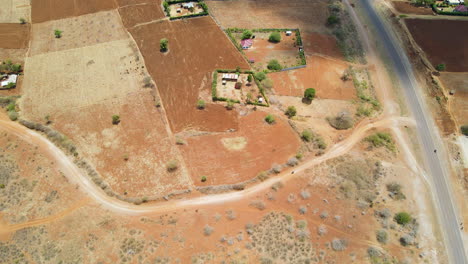 Aerial-of-bike-driving-over-dirt-road-near-a-motorway-in-rural-Kenya