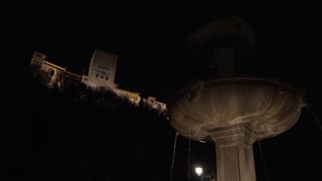 Blick-Auf-Die-Alhambra-Während-Der-Nacht-Von-Unten-Mit-Einem-Brunnen-Und-Schönen-Lichtreflexionen-Des-Wassers