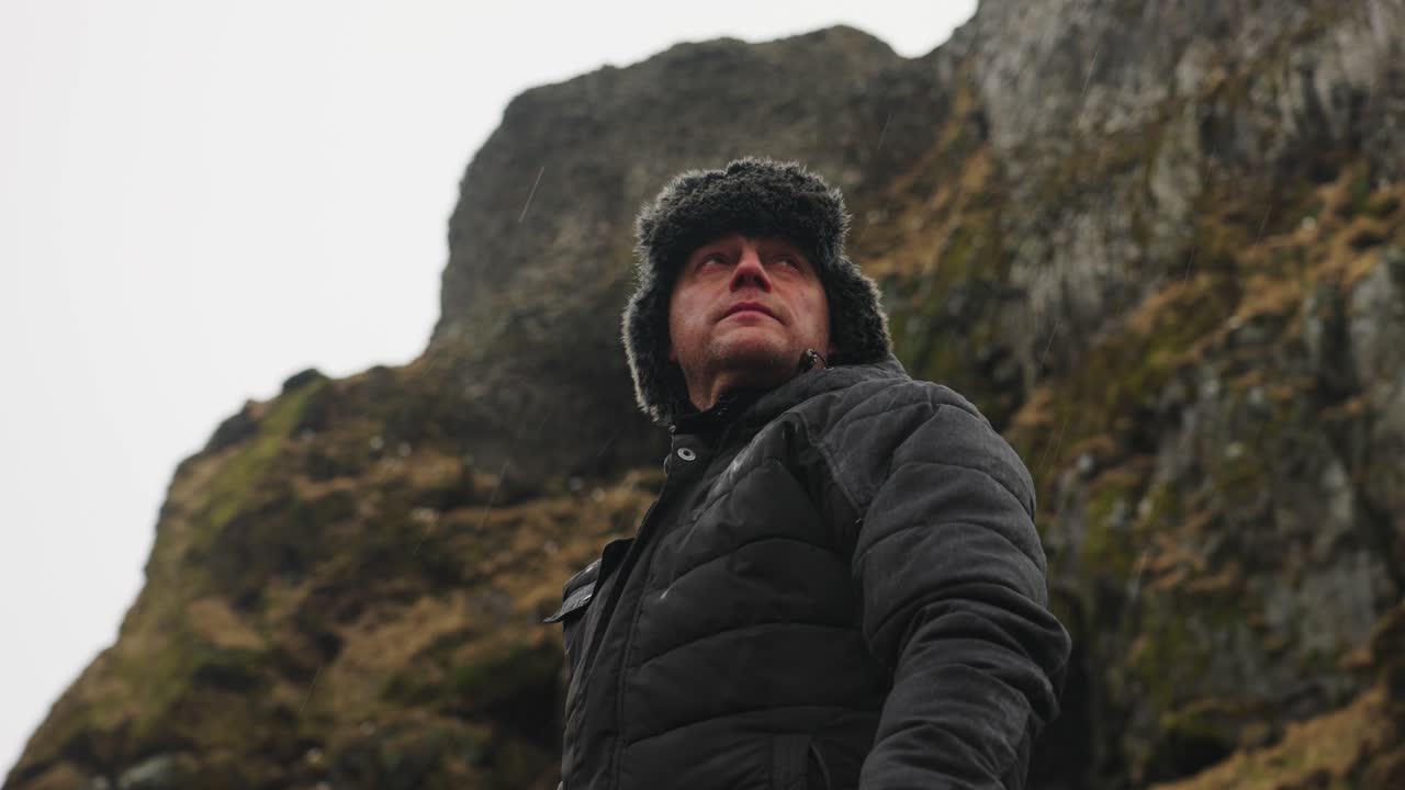 el turista masculino se encuentra en un paisaje montañoso islandés lluvioso con un cielo brillante