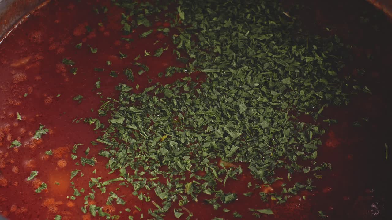 primer plano de agregar perejil al guiso de sopa humeante y revolver con una cuchara de madera