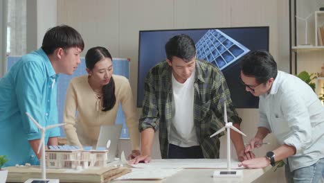 grupo de ingenieros asiáticos con el modelo de casa de paneles solares abriendo el plan y luego discutiendo sobre el trabajo en la oficina