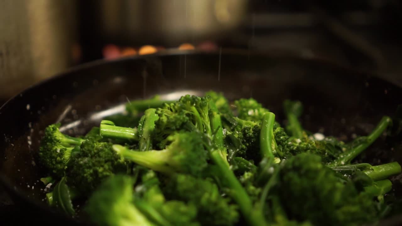 Close Up - Sprinkling salt on steamed fresh green broccoli on a black frying pan