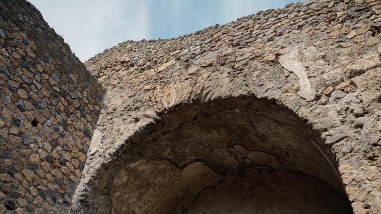 Vista dal basso di una nicchia a volta crepata a Pompei, che evidenzia la muratura romana curva, l'intonaco antico e il degrado strutturale all'interno delle rovine archeologiche.