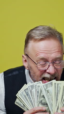 happy old man with dollars in his hands. positive rich man demonstrates his money. face of a funny senior man with money. close-up. vertical video