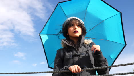 mujer joven con paraguas azul y cielo preparándose para una tormenta de lluvia después de comprobar el tiempo en cámara lenta