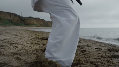 closeup legs sporty man exercising sandy beach. karate fighter doing workout.