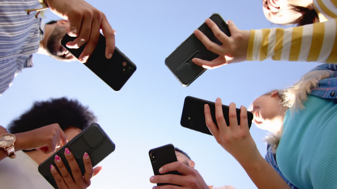 Friends holding smartphones, taking photos and enjoying time together outdoors