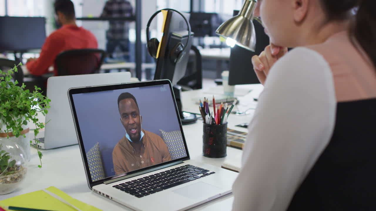 Caucasian woman having a video call with male office colleague on laptop at office
