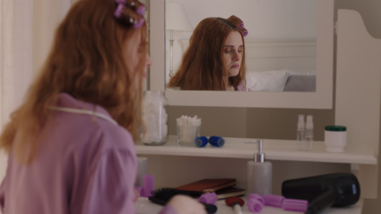 행복한 십대 소녀가 헤어 드라이어를 사용하고 준비하고 거울을 보며 주말 아침에 나갈 준비를 하고 있습니다.