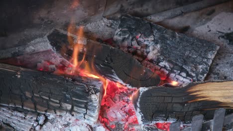 black charred wooden logs in ash filled fireplace, small orange flames