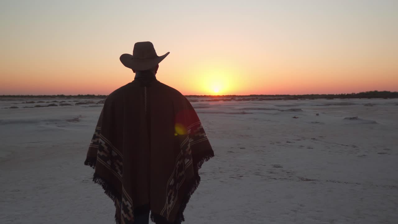 해돋이를 보고 있는 소금밭에 서 있는 카우보이 복장을 한 남자의 돌리 샷