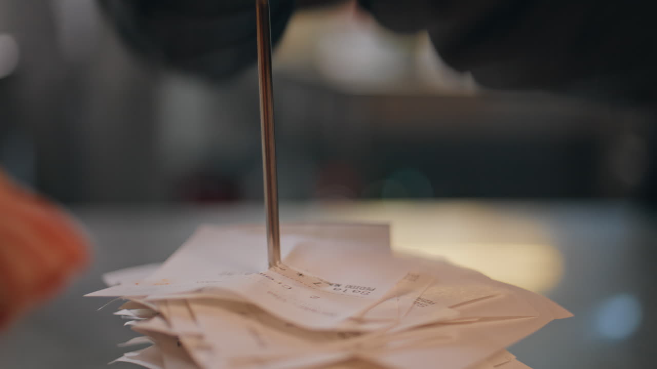 Nærbillede af regninger spiddet på en spids i et travlt restaurantkøkken. Papirkvitteringer stablet.
