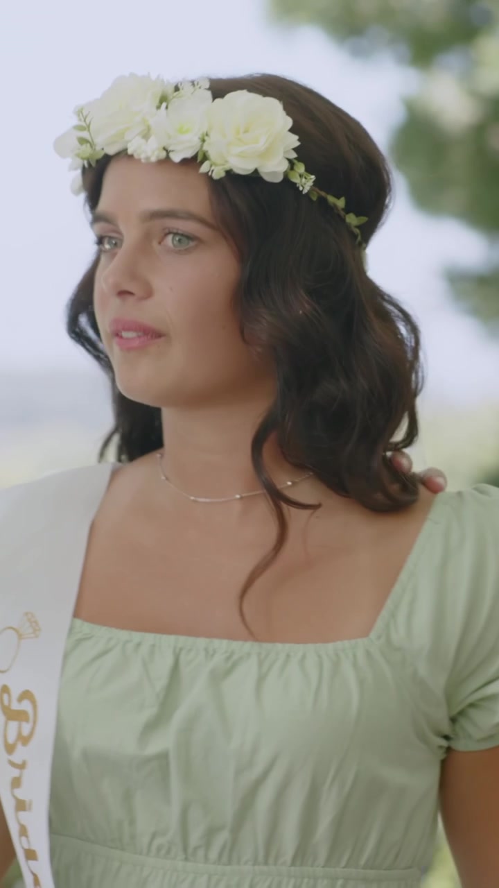 Vertical video: Female pals moving, placing flower crown and draping sash in yard, toasting bride