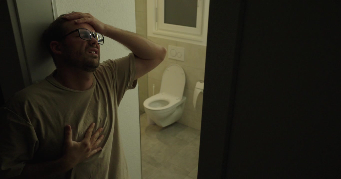 Man holding his chest and appearing unwell near a bathroom. Concept of nausea, illness, stomach discomfort, health problems, and medical emergency symptoms.