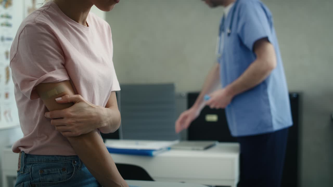 Caucasian female patient with adhesive bandage on her arm just right after vaccination and doctor in the background