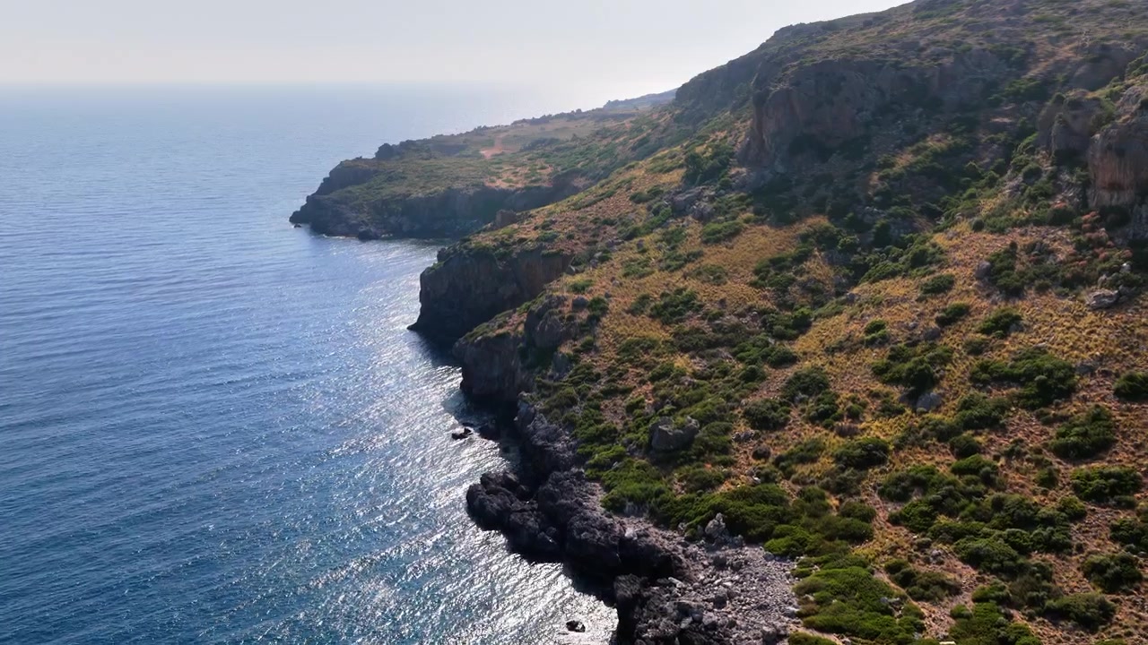 Vista aerea con drone di ripide scogliere frastagliate che si tuffano nel calmo mare blu lungo una costa velata, Creta, Grecia