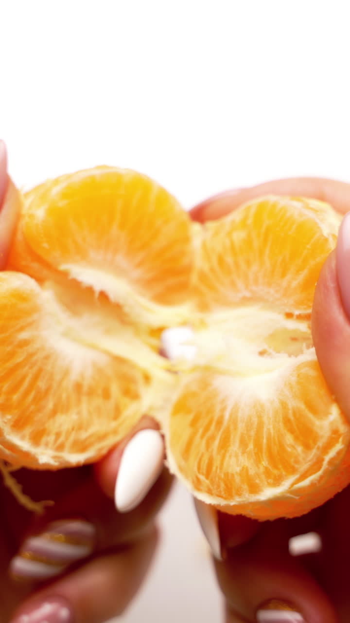 Orange mandarin in woman's hands. Hands are peeling a juicy fruit on white background. Close-up. Vertical video