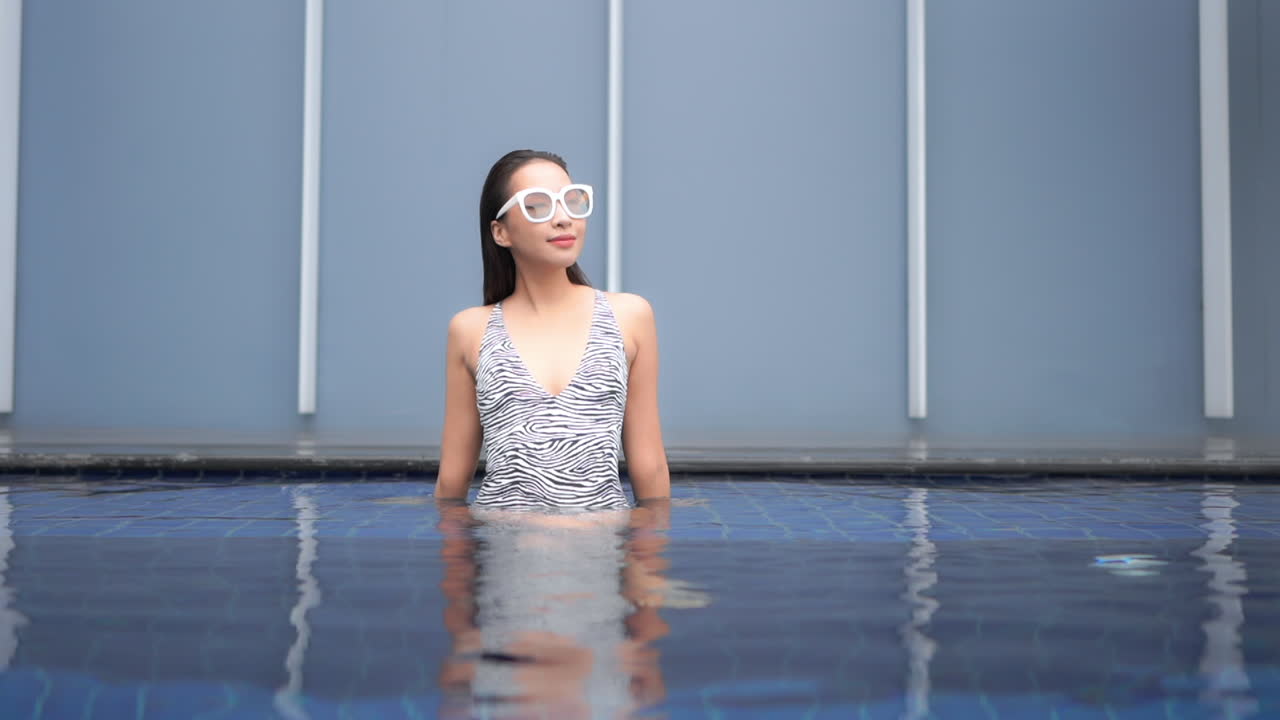 Classy petite asian female enjoying in pool of luxury hotel resort, slow motion. Full frame static view with copy space