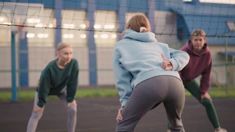 back view of ladies slightly bent with lady in blue hoodie making hand gesture while other two ladies watch her attentively during an outdoor physical activity session