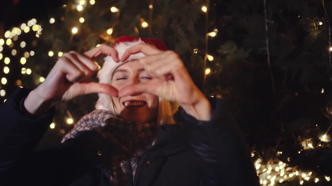 Donna festeggia il Natale, sorridendo e mostrando la forma di un cuore con le mani