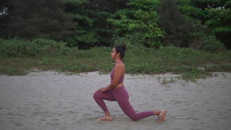 Indian-Yoga-Girl-in-Nature-Doing-Lunge-Stretches-on-Beach-Sand-at-Dusk,-Dawn