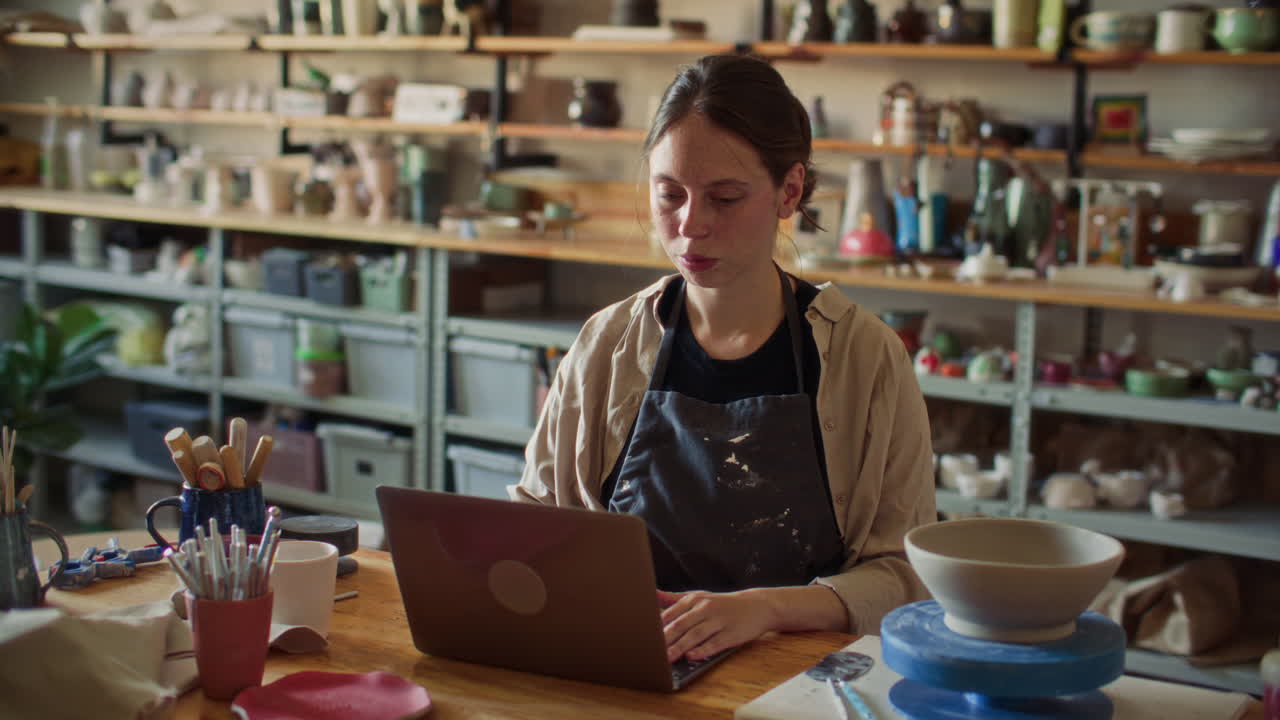 Female Ceramic Artist Working on Laptop in Pottery Studio
