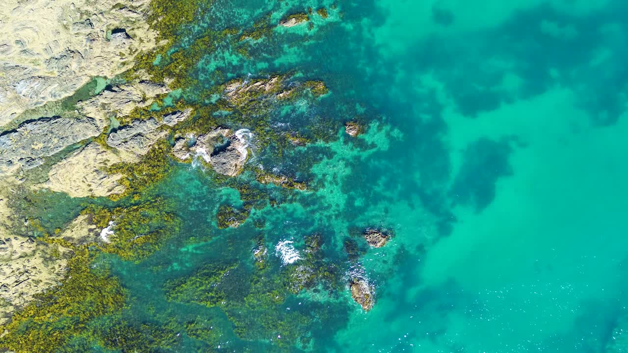 Batemans Körfezi Avustralya seyahat turizmi tatilleri doğasında, yosunla kaplı kayalıkların üzerinde kırılan dalgaların ve kıyı şeridindeki burun boyunca uzanan resif okyanusu kum setinin drone ile çekilmiş havadan manzarası