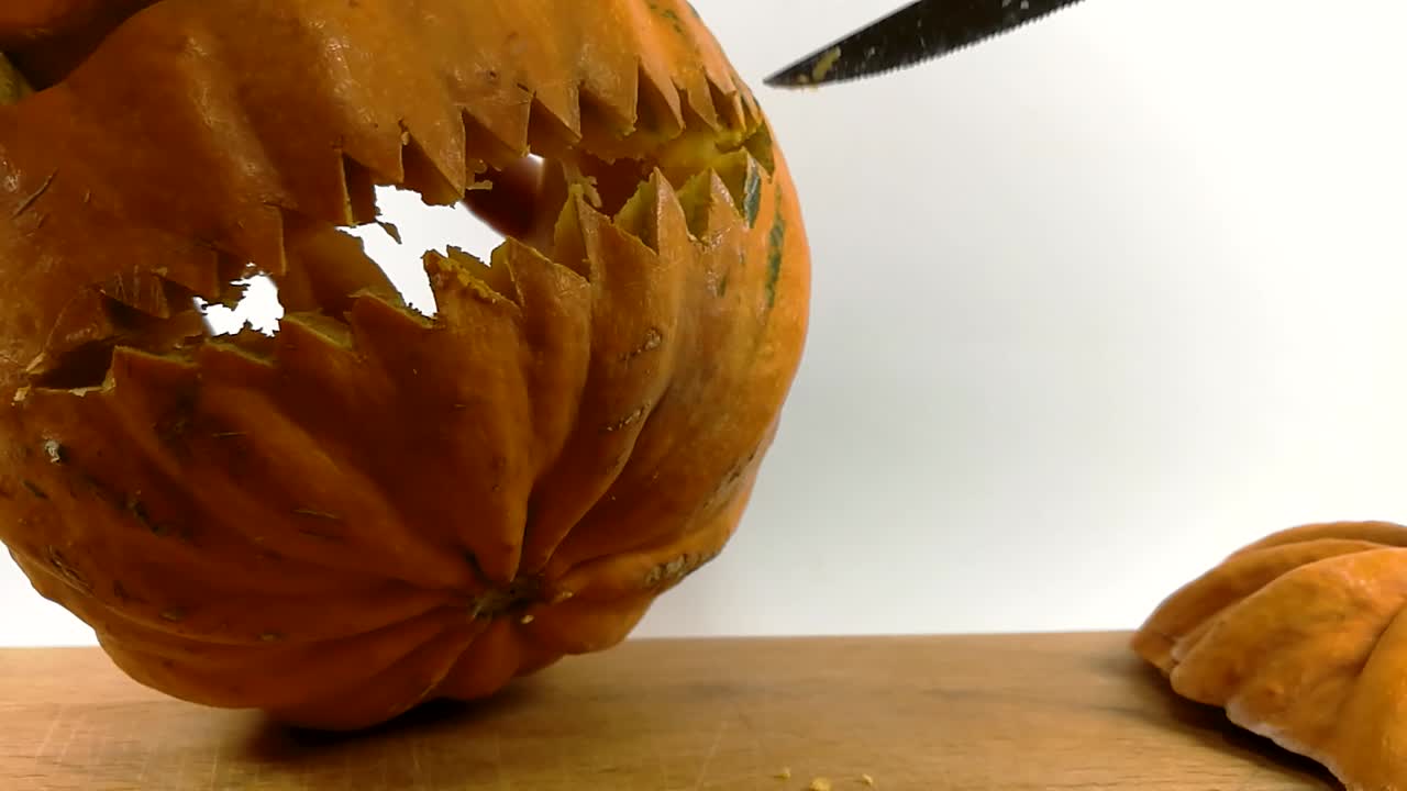 tallado de calabaza parte 12, persona terminando tallado de pequeños dientes puntiagudos en calabaza de halloween con un pequeño cuchillo dentado puntiagudo en la tabla de cortar de madera, todavía, aislado, slomo