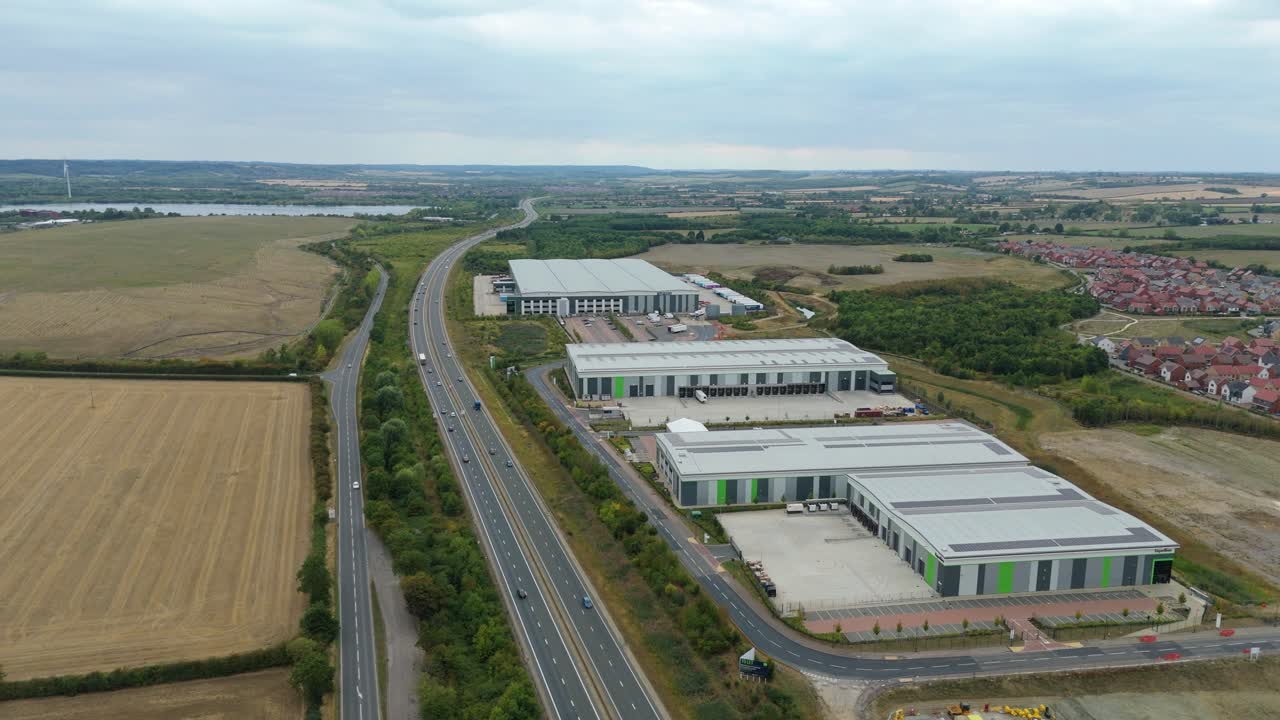Aerial drone footage of Bedford England motorway junction with busy highway transport and surrounding industrial warehouses, factories and distribution