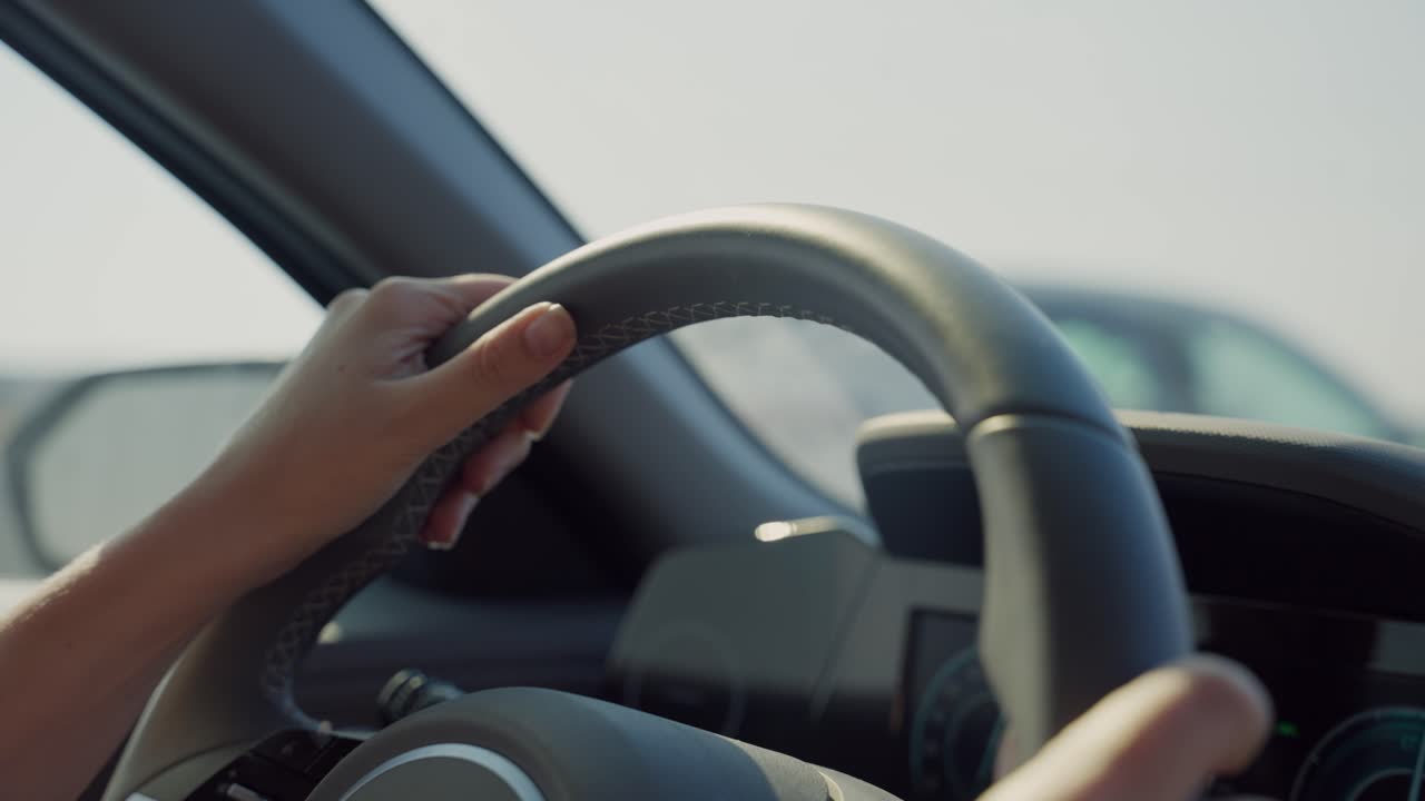 Female hands holding steering wheel driving vehicle or modern sedan car in highway. Car ride as woman commuting to work or going for vacation on sunny day sun shining into dashboard as cars pass by