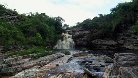 Tilting-up-4K-shot-revealing-the-stunning-Devil's-Pit-waterfall-surrounded-by-foliage-and-rocks-on-an-overcast-rainy-day-in-the-famous-Chapada-Diamantina-National-Park-in-Northeastern-Brazil