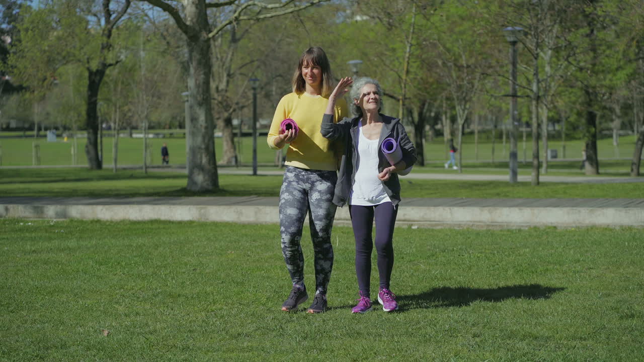vista frontal de las mujeres en el parque sosteniendo el tapete de yoga en las manos, hablando