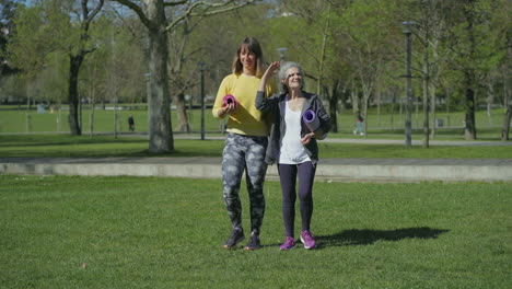 front view of women in park holding yoga mat in hands, talking