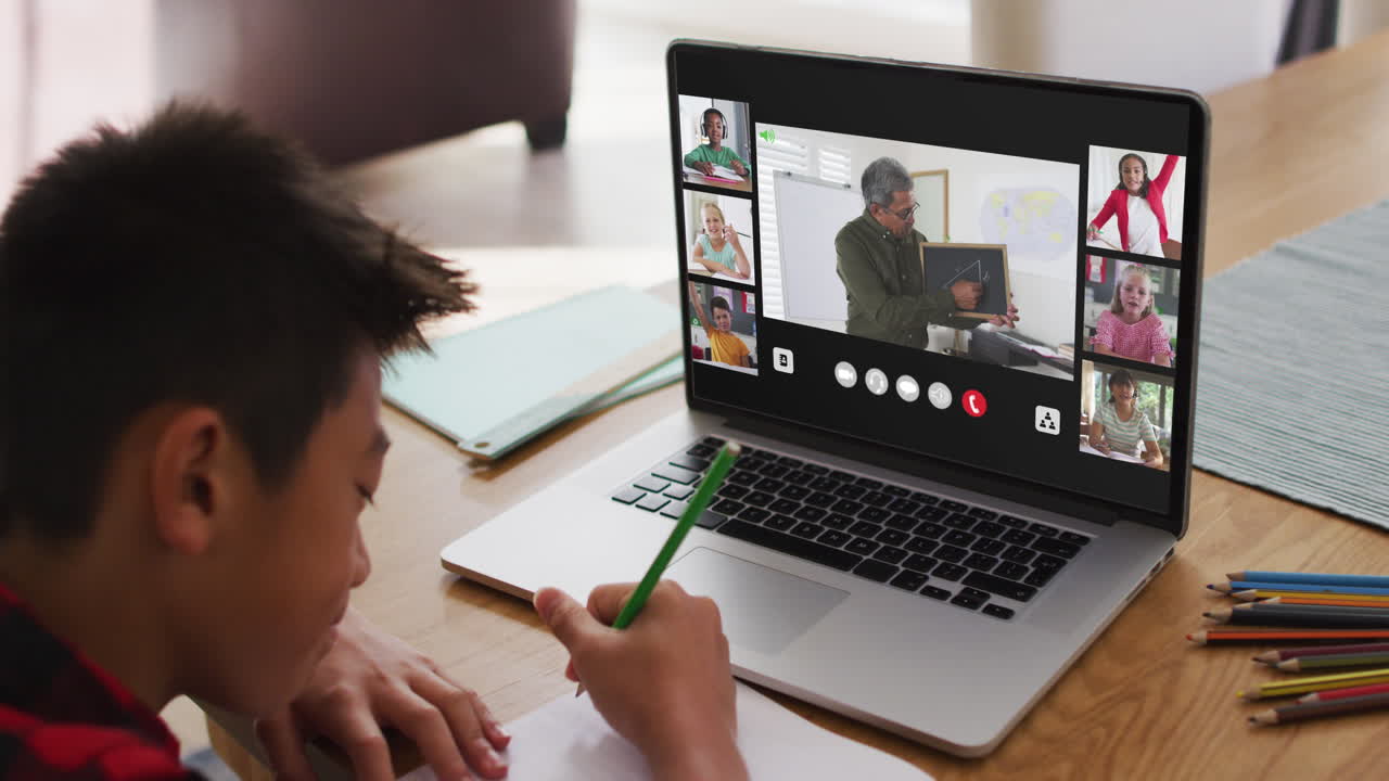 Schoolboy using laptop for online lesson at home, with diverse teacher and class on screen