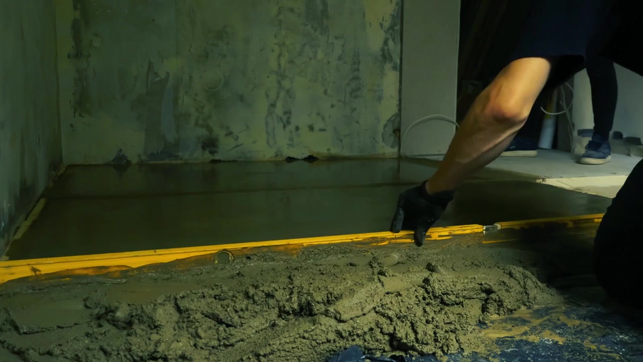 Professional builder installing a new cement screed floor during a home renovation, using a spirit level to carefully smooth and flatten the fresh mixture before it sets and hardens, timelapse