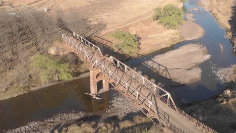 Toma-Aérea-De-Un-Ciclista-De-Montaña-Cruzando-Un-Viejo-Puente-De-Acero.