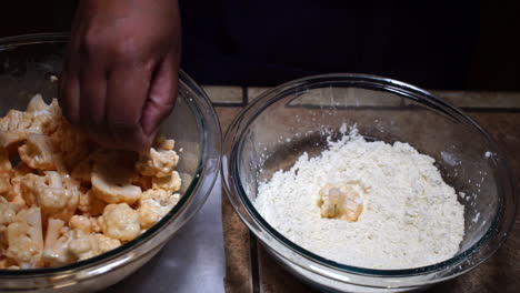 person dropping cauliflower with sauce into flour for breading, slow motion