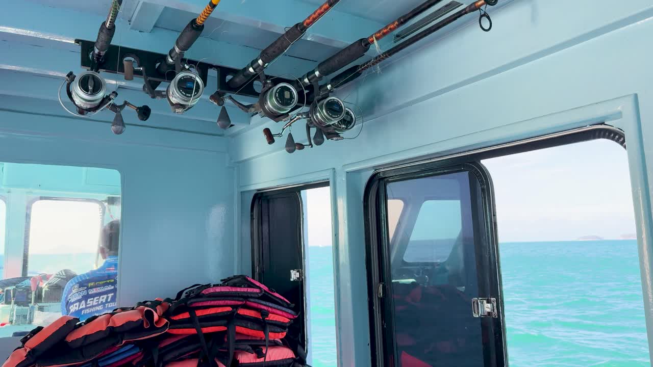 Interior of a fishing boat with life jackets and rods, navigating through the ocean near Phuket, Thailand. Bright daylight illuminates the scene