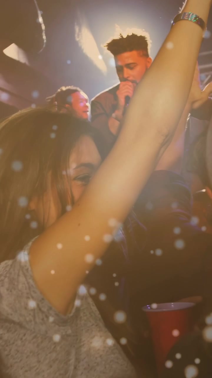 Video verticale: Fan che balla alzando le braccia in un locale di musica mentre il cantante fa apparire scintille che si sovrappongono alla scena.