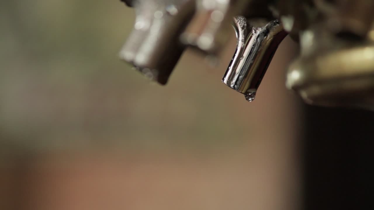 Rekaman close-up dari cerat portafilter mesin espresso metalik dengan tetesan cairan menggantung di ujungnya. Latar belakang yang buram menonjolkan cerat dan tetesan tersebut, menangkap momen yang presisi.