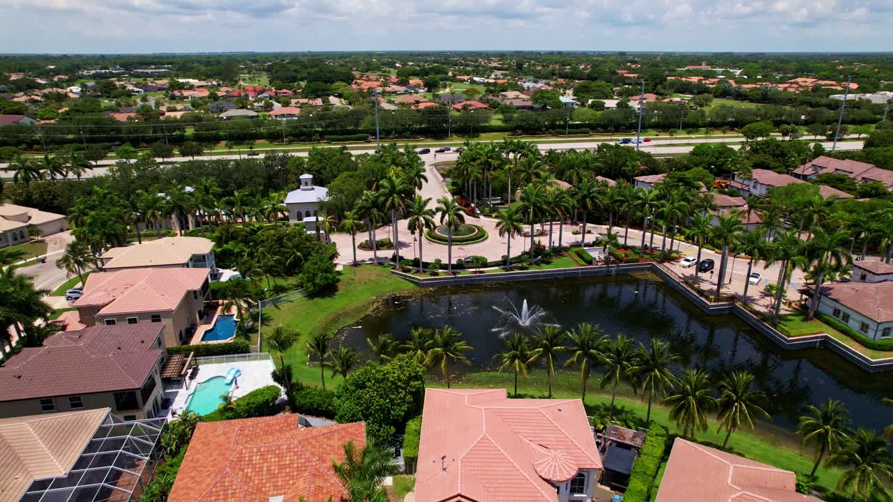Aerial: residential area and lake during the day with cloudy weather and palm trees in West Palm Beach, Florida, USA, establishing drone shot