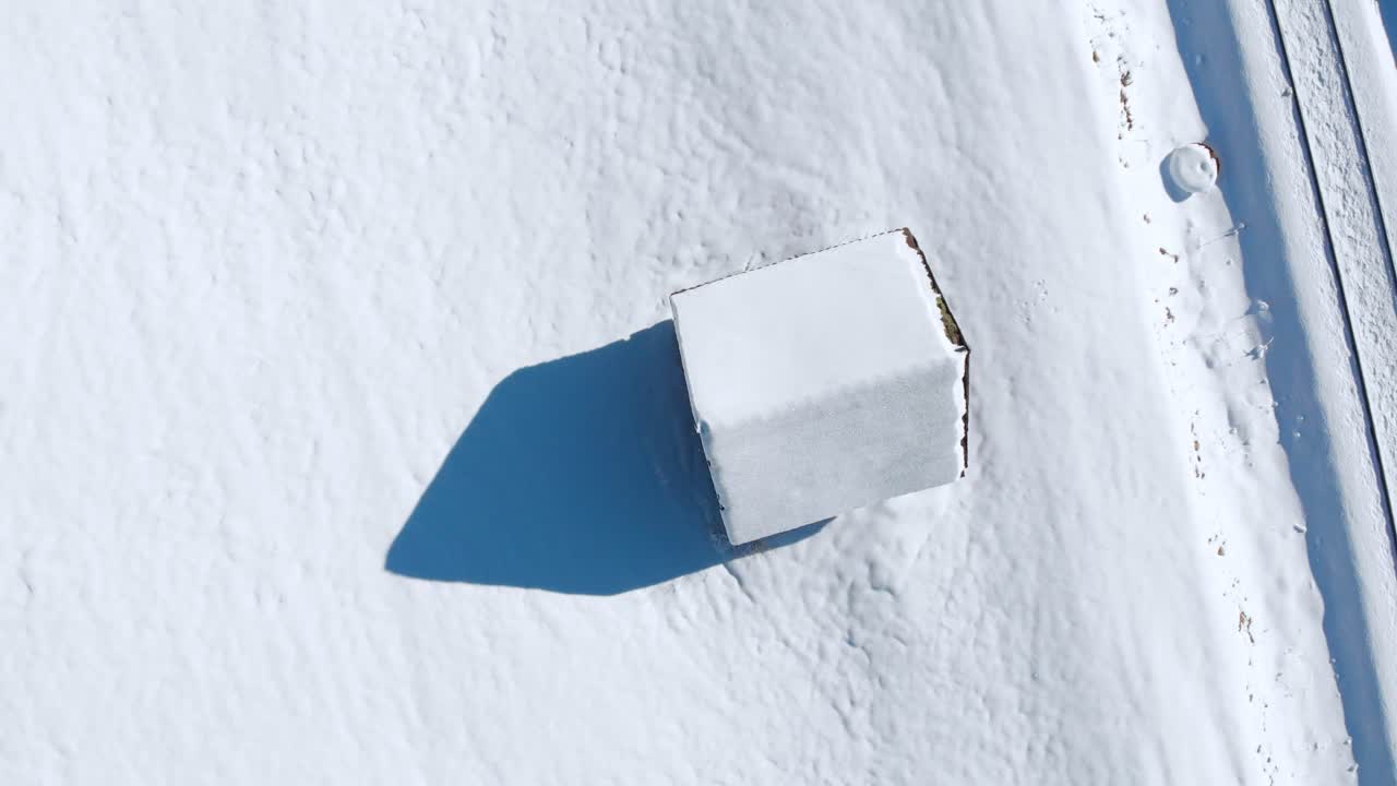 Aerial: zenital shot of a snowy cabin in the Alps, descending shot