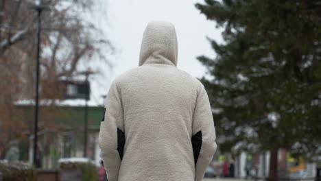 vista trasera de una persona con una chaqueta blanca de invierno paseando, con un fondo borroso que muestra un entorno urbano ocupado, evocando una sensación de soledad en medio de la vida de la ciudad