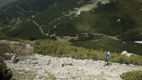 seguimiento lateral desde arriba de un excursionista caminando por un camino rocoso en la montaña snežnik, ayudándose a sí mismo a caminar con bastones de senderismo