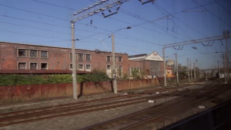 slowly moving train going down tracks and looking out window at old run down industrial building