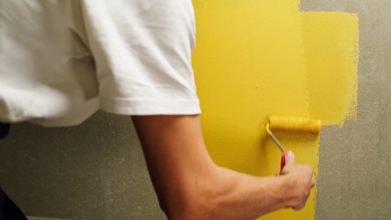 Persona che applica pittura gialla alla parete con un rullo
